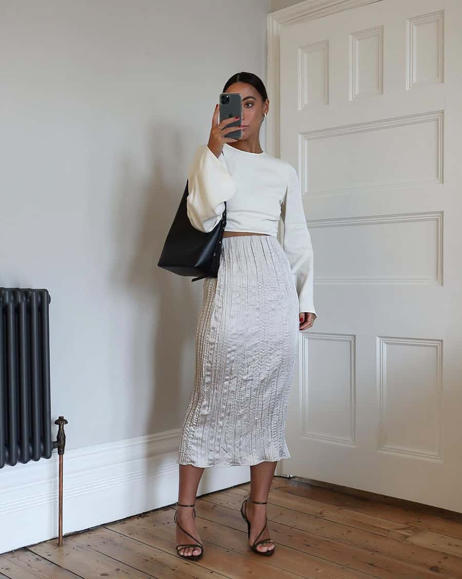 woman wearing a cropped white blouse with a pleated silk midi skirt and heels
