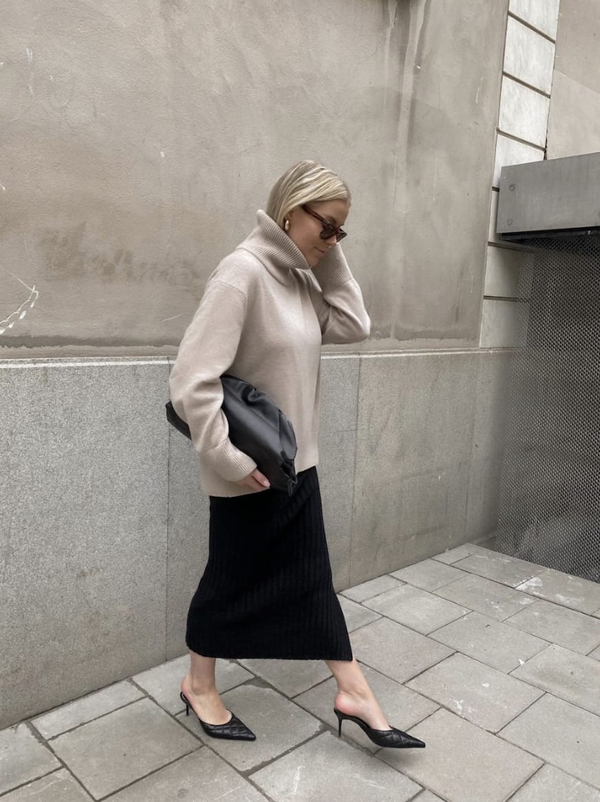 woman wearing an oversized neutral turtleneck with a black midi skirt and low black pumps