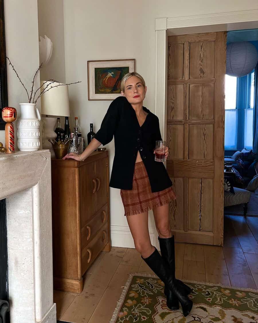 woman wearing a black button front cardigan with a plaid mini skirt and knee high boots