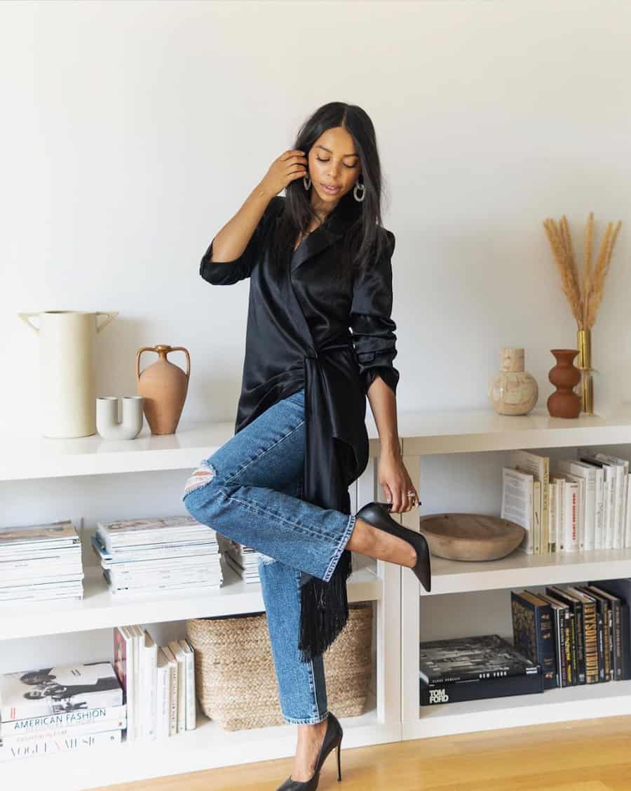 black woman wearing a long black silk blouse with jeans and black pumps