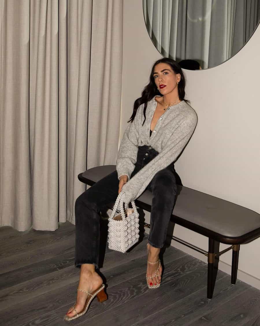 woman wearing a grey knit cardigan sweater tucked into black jeans with heeled sandals