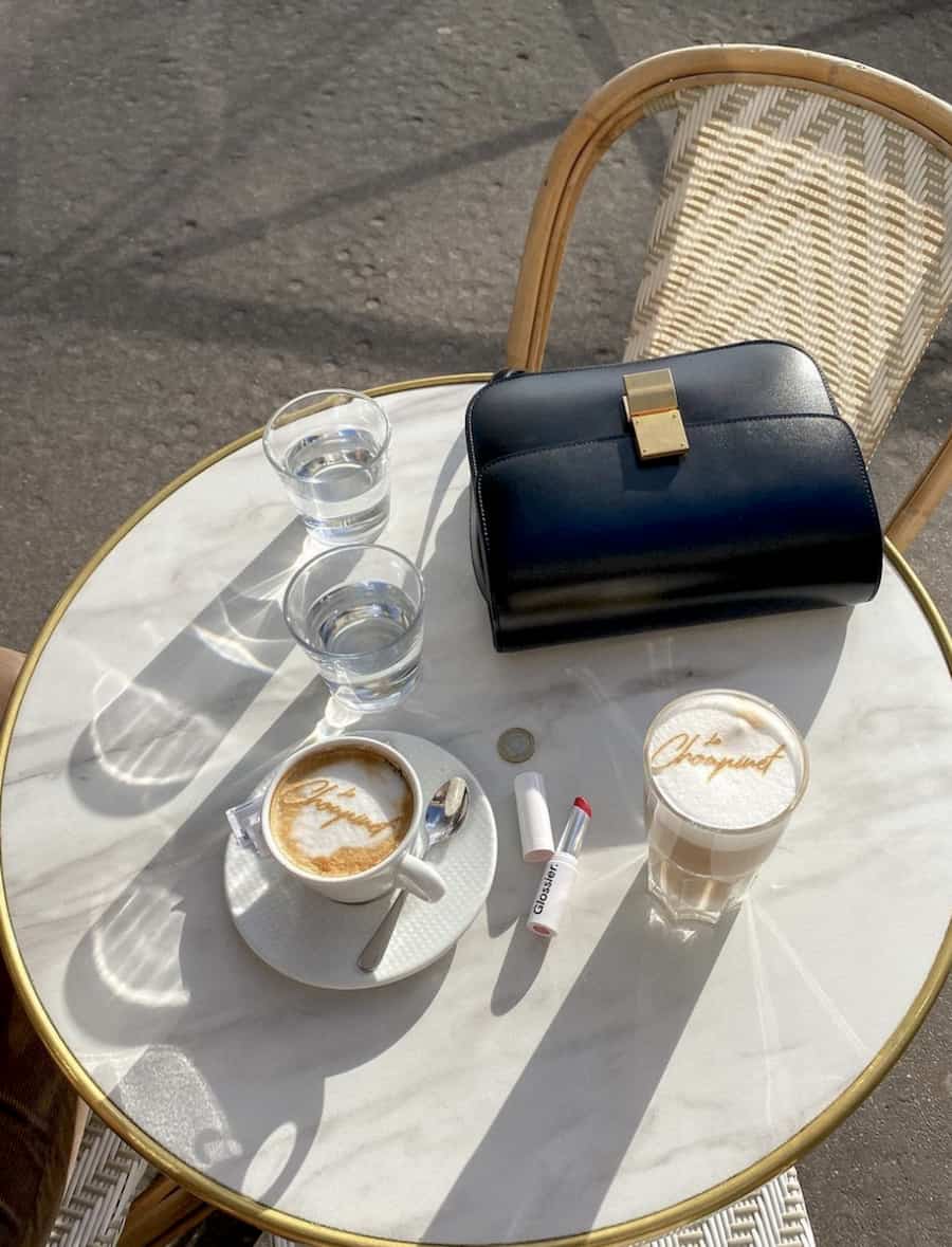 a black Celine box bag sitting on a white marble cafe table with coffee cups on it