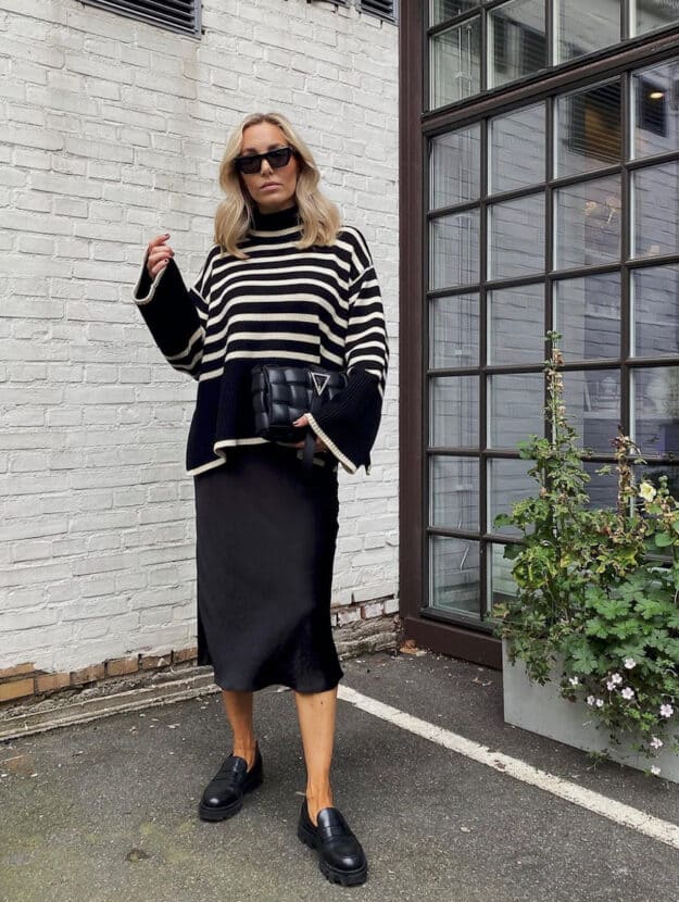 image of a woman wearing an oversized striped black and white turtleneck sweater with a black silk midi skirt and chic black loafers