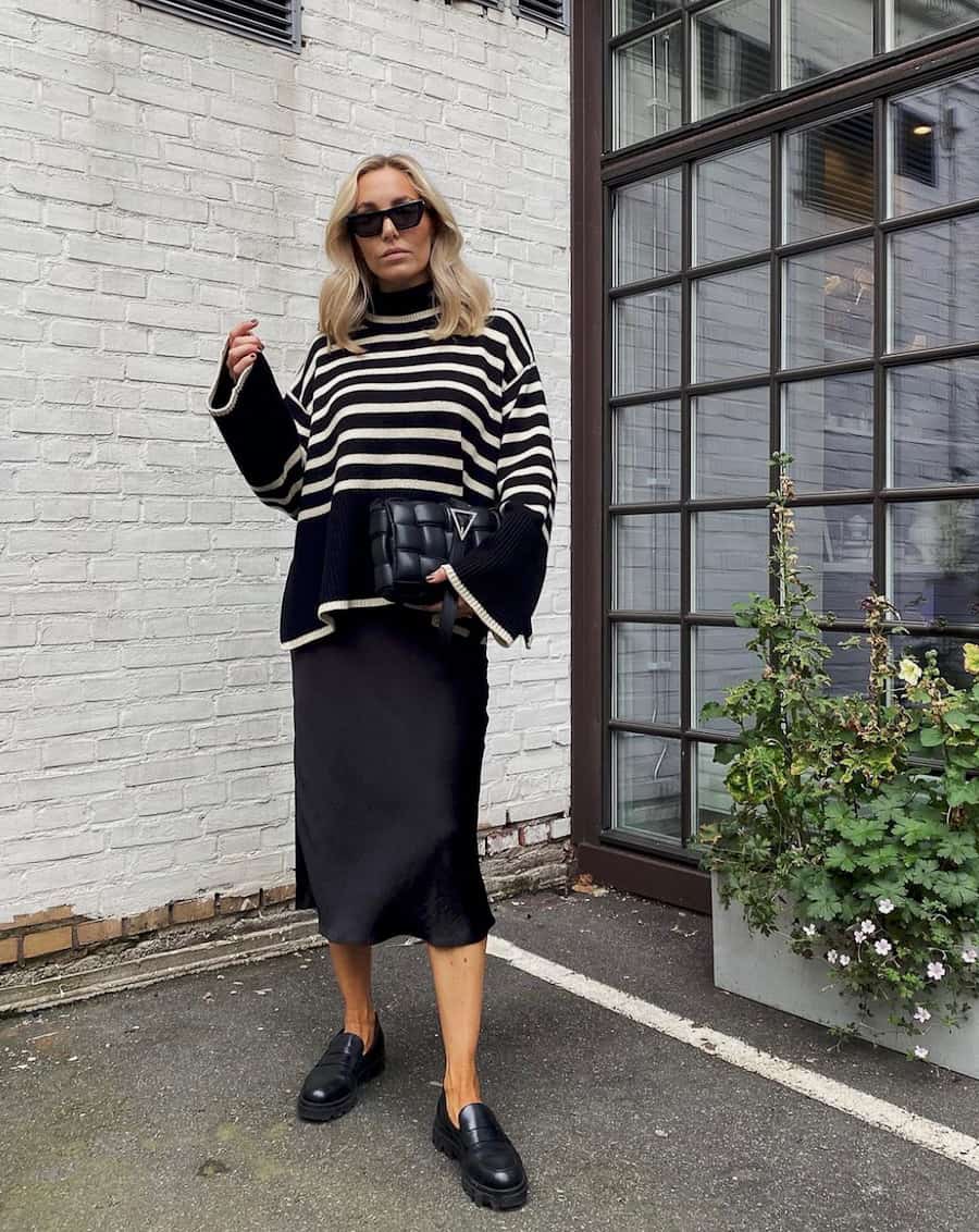 image of a woman wearing an oversized striped black and white turtleneck sweater with a black silk midi skirt and chic black loafers