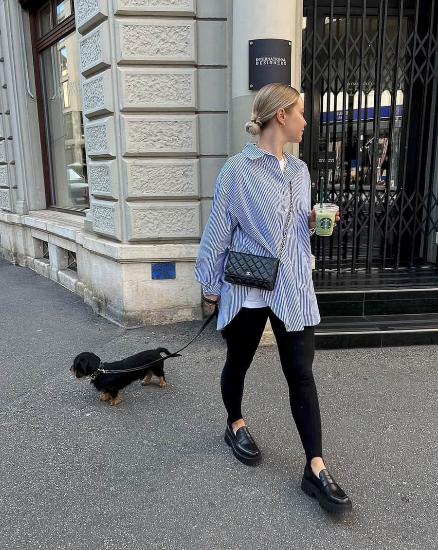 image of a woman walking her dog wearing a striped oversized button up shirt, black leggings with stirrup detail and black chunky style loafers