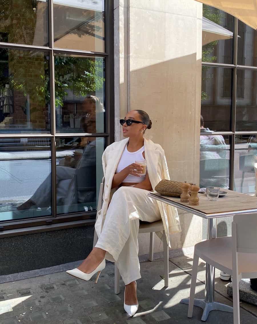 woman sitting at a coffee shop patio wearing a linen pant suit and white pumps