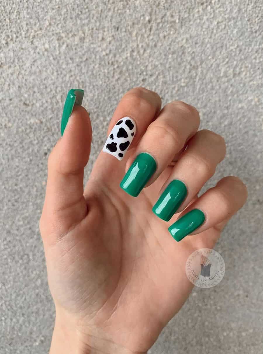 a hand with bold green nails and one cow print accent nail in black and white