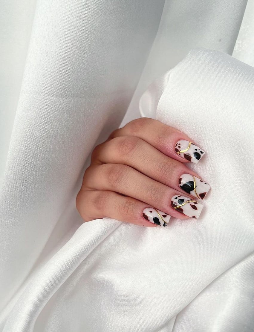 a hand with white nails with a cow print and gold design detail