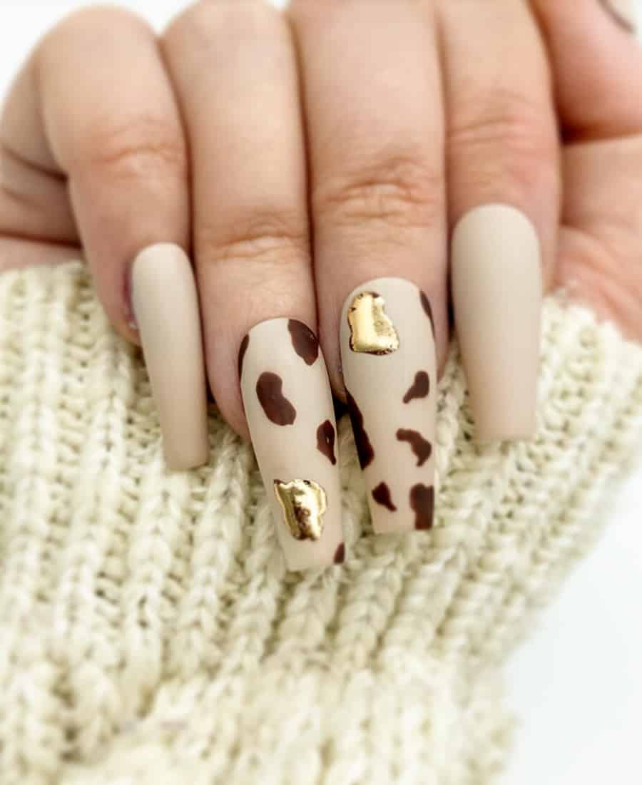 a hand with beige matte nails with a molten gold accent and brown cow print design