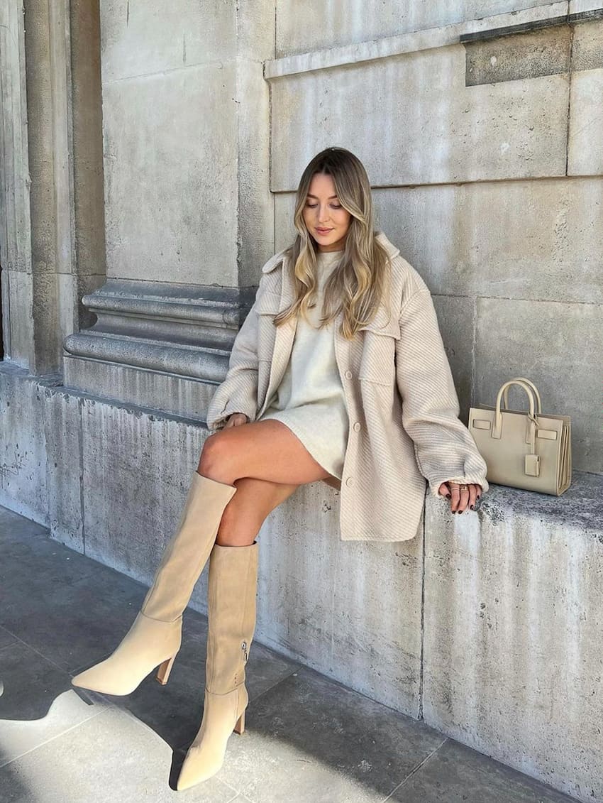 woman wearing a beige wool shirt jacket, cream sweater dress, and suede knee-high boots