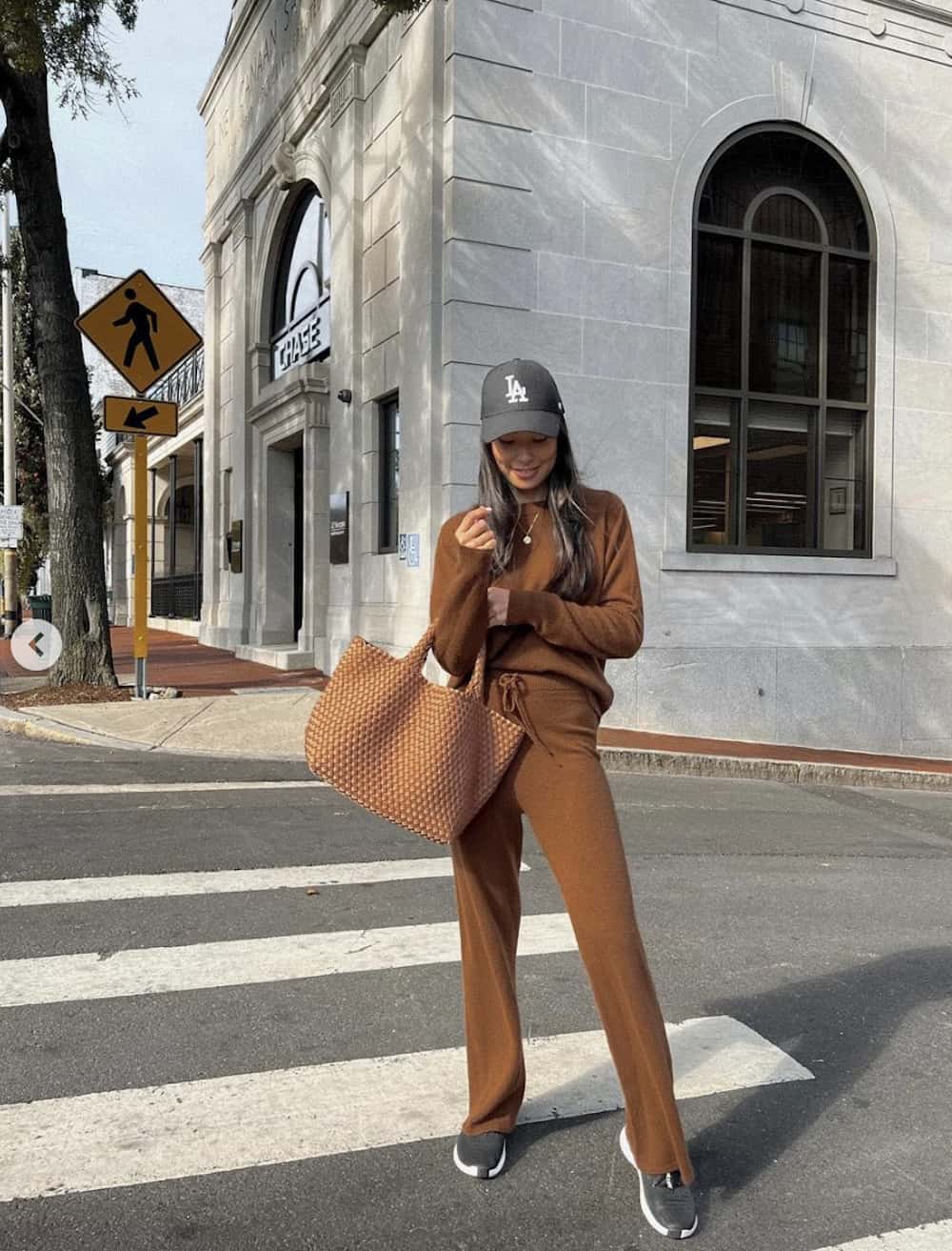 Woman wearing a matching rust colored sweat set with a Los Angeles hat.