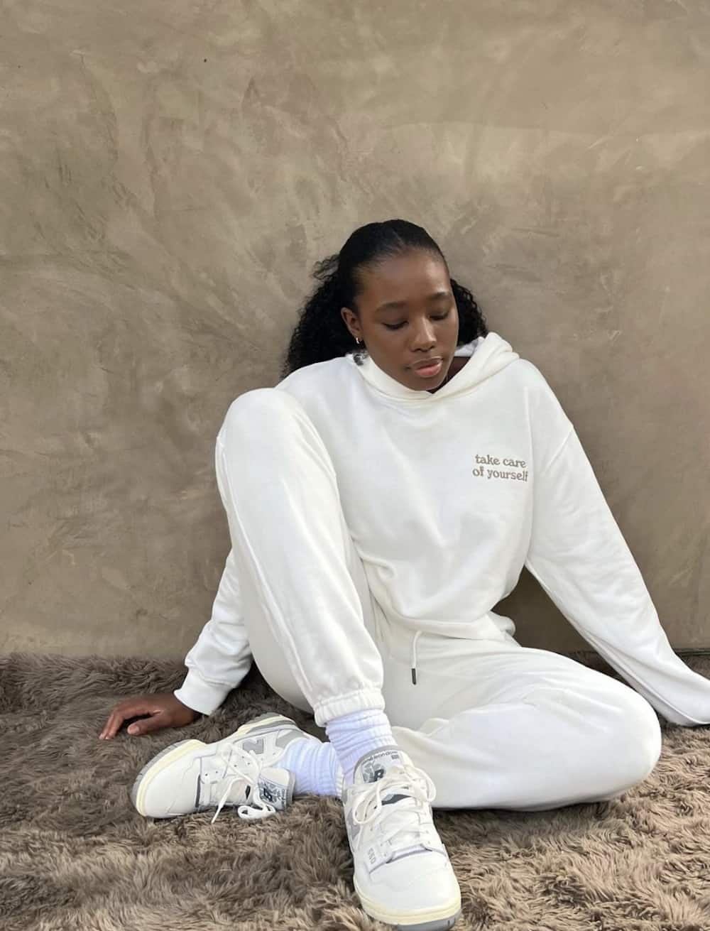 Woman wearing a matching white sweat set with white sneakers.