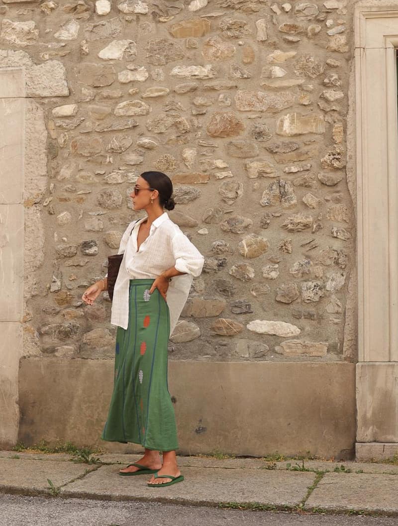 woman wearing a flowy white button up shirt with a green midi length printed skirt and sandals