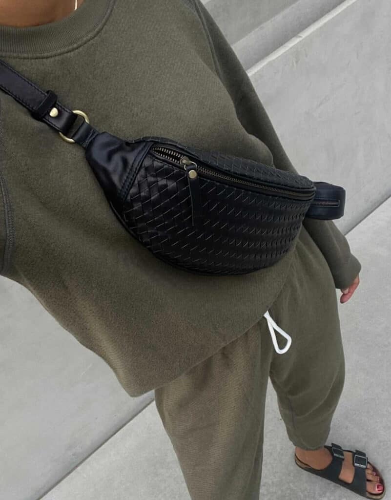 image of a woman wearing a matching olive green sweatsuit and a black woven leather fanny pack