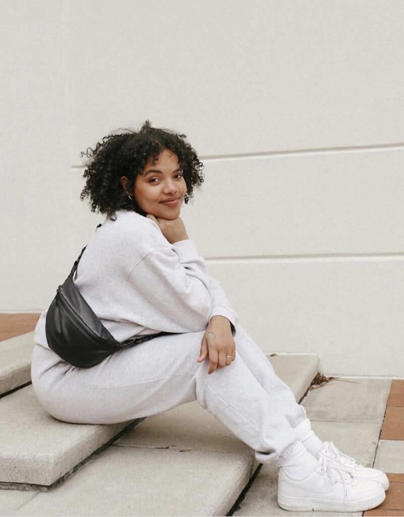image of a black woman wearing a matching heather grey sweatsuit and a black fanny pack slung over her shoulder