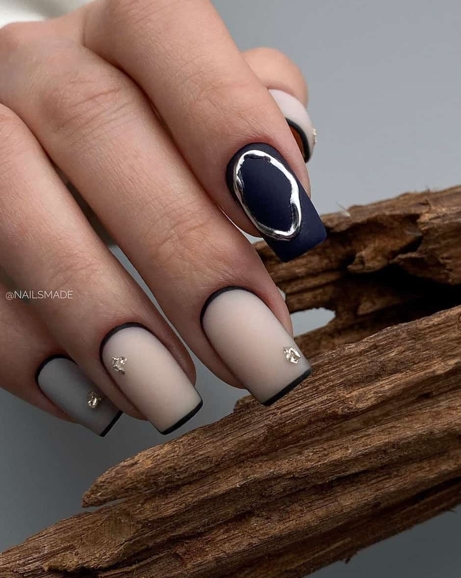 hand with natural nails and a dark navy blue nail with gold ring accent