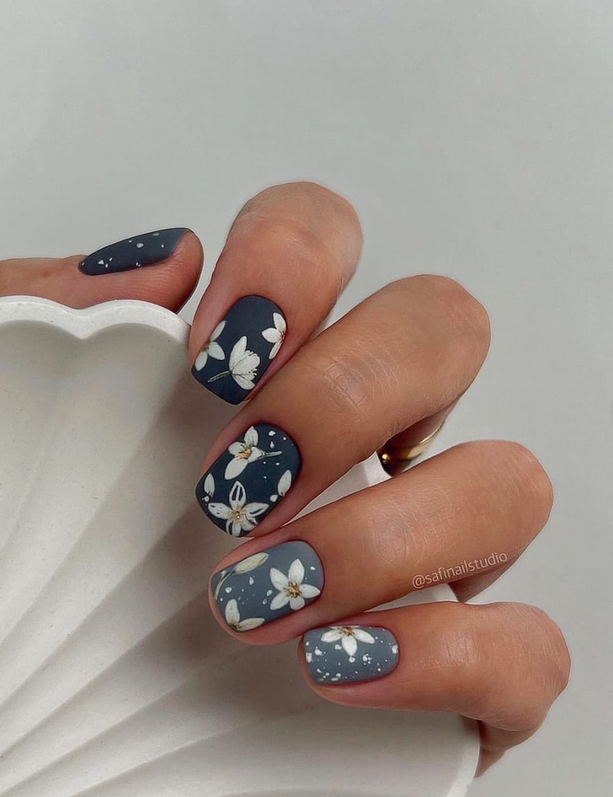 hand with dark and medium blue nails with daisy art