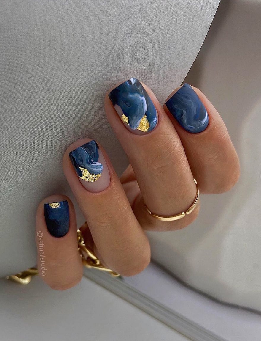hand with dark blue mail polish with gold accents