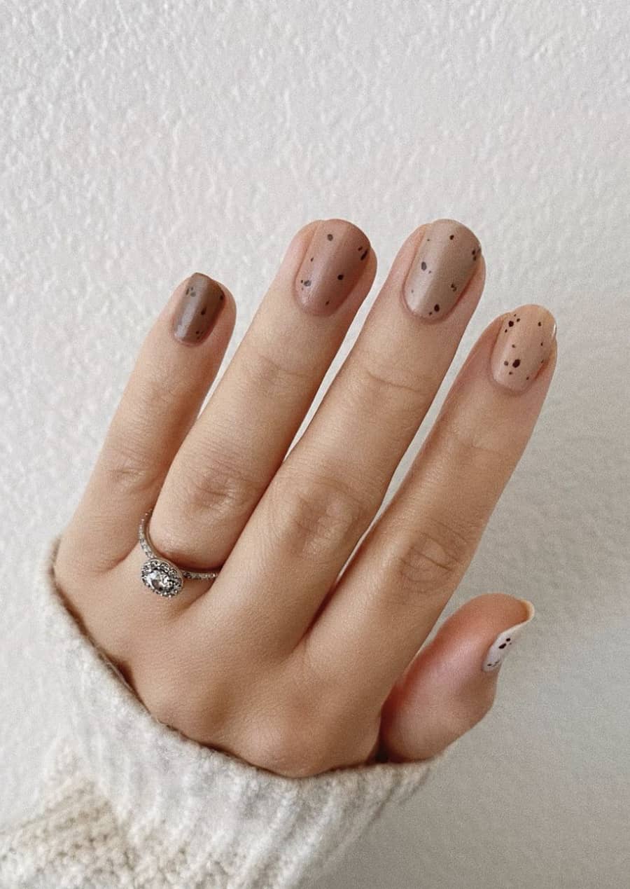 image of a hand with short ombre brown nails with black speckles
