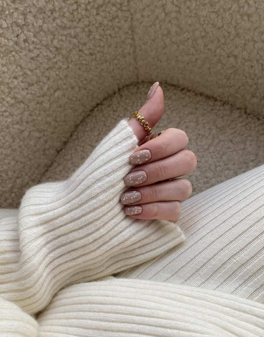 image of a woman's arm in a cream sweater, her hand with short white and brown speckled nails