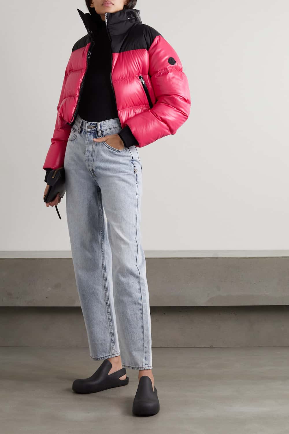 woman wearing a black sweater with a hot pink puffer jacket and light blue jeans