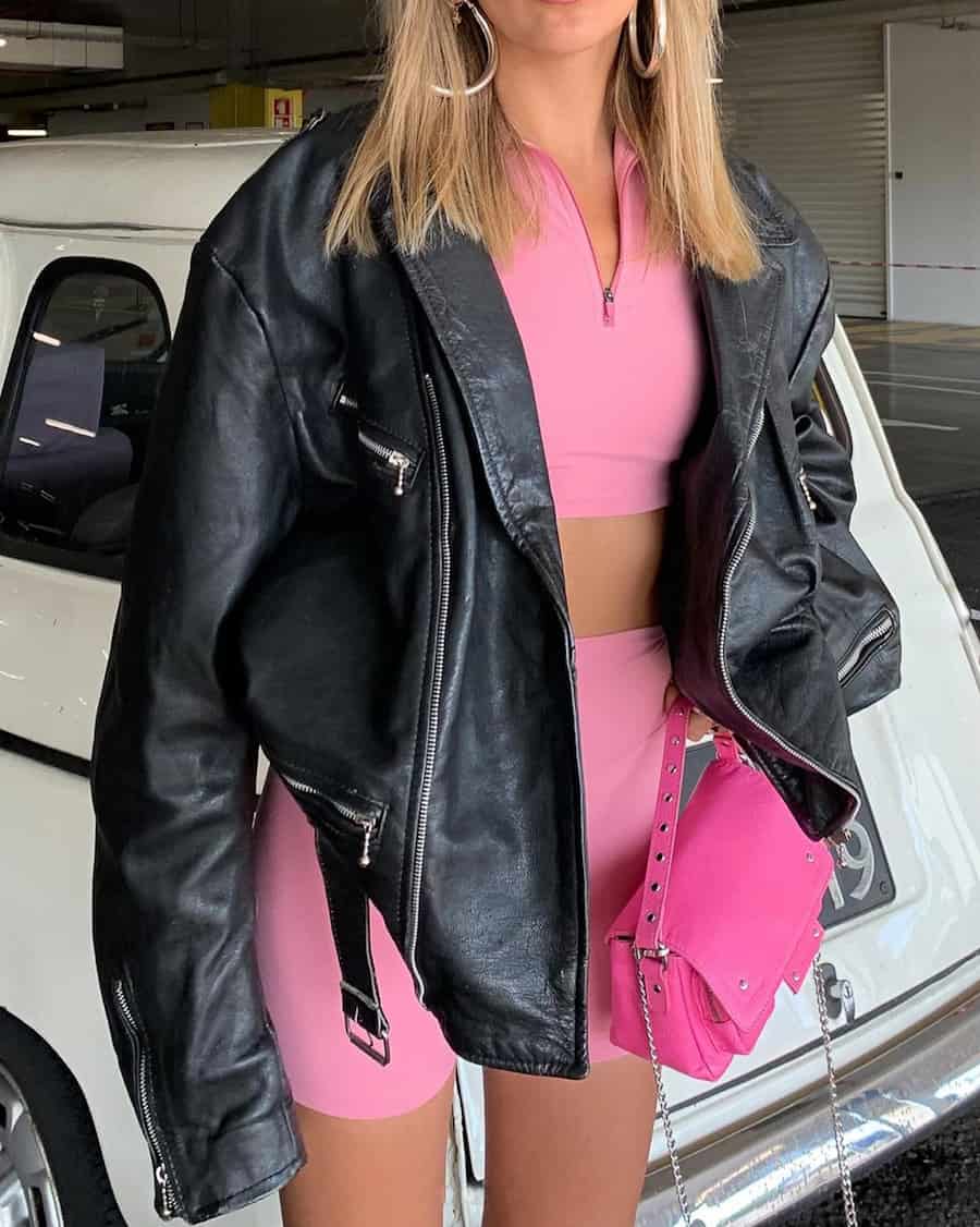 woman wearing a pink matching shorts and crop top with black leather jacket
