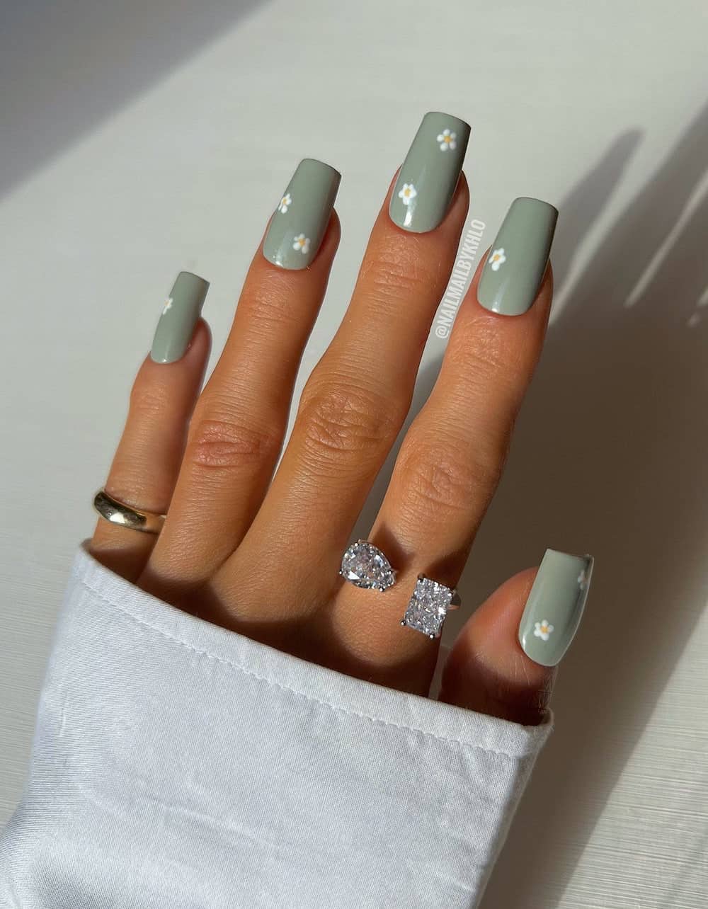 hand with long acrylic sage green nails with white flowers