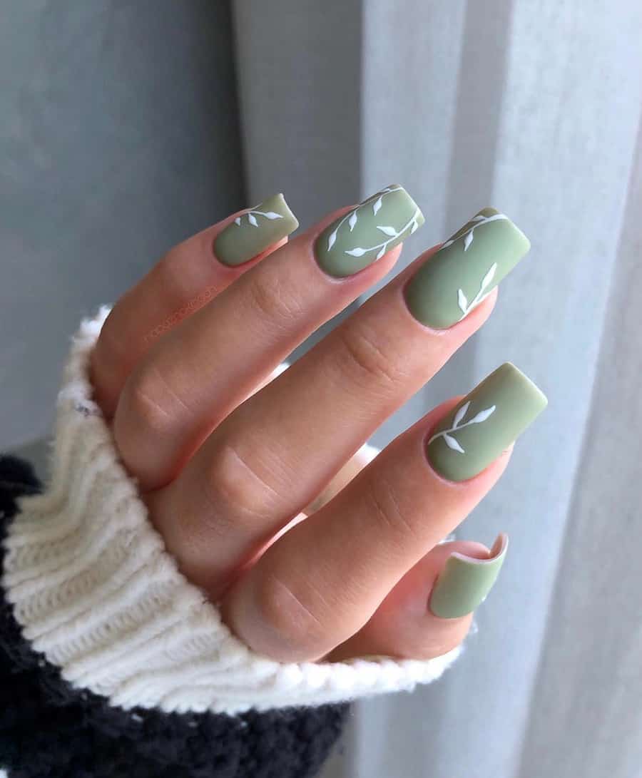 hand with light sage green polish and white leaf accents