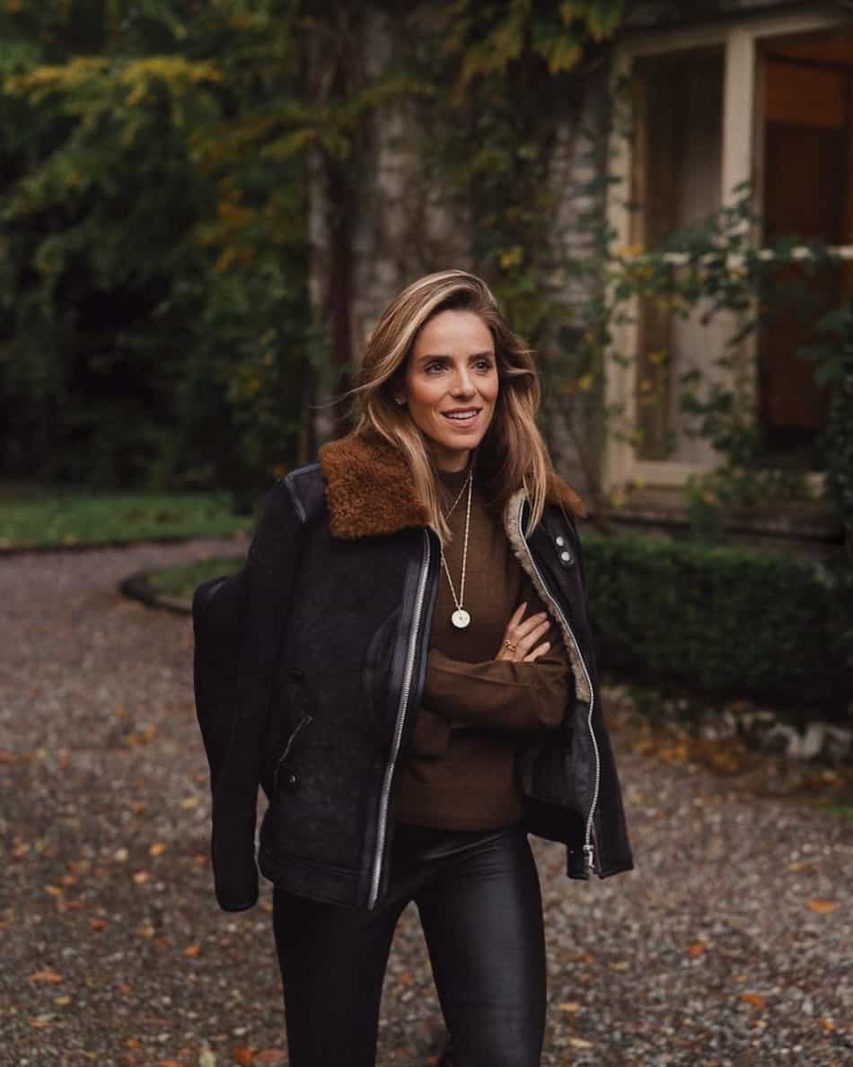 woman wearing a black leather shearling-lined coat with a brown knit sweater