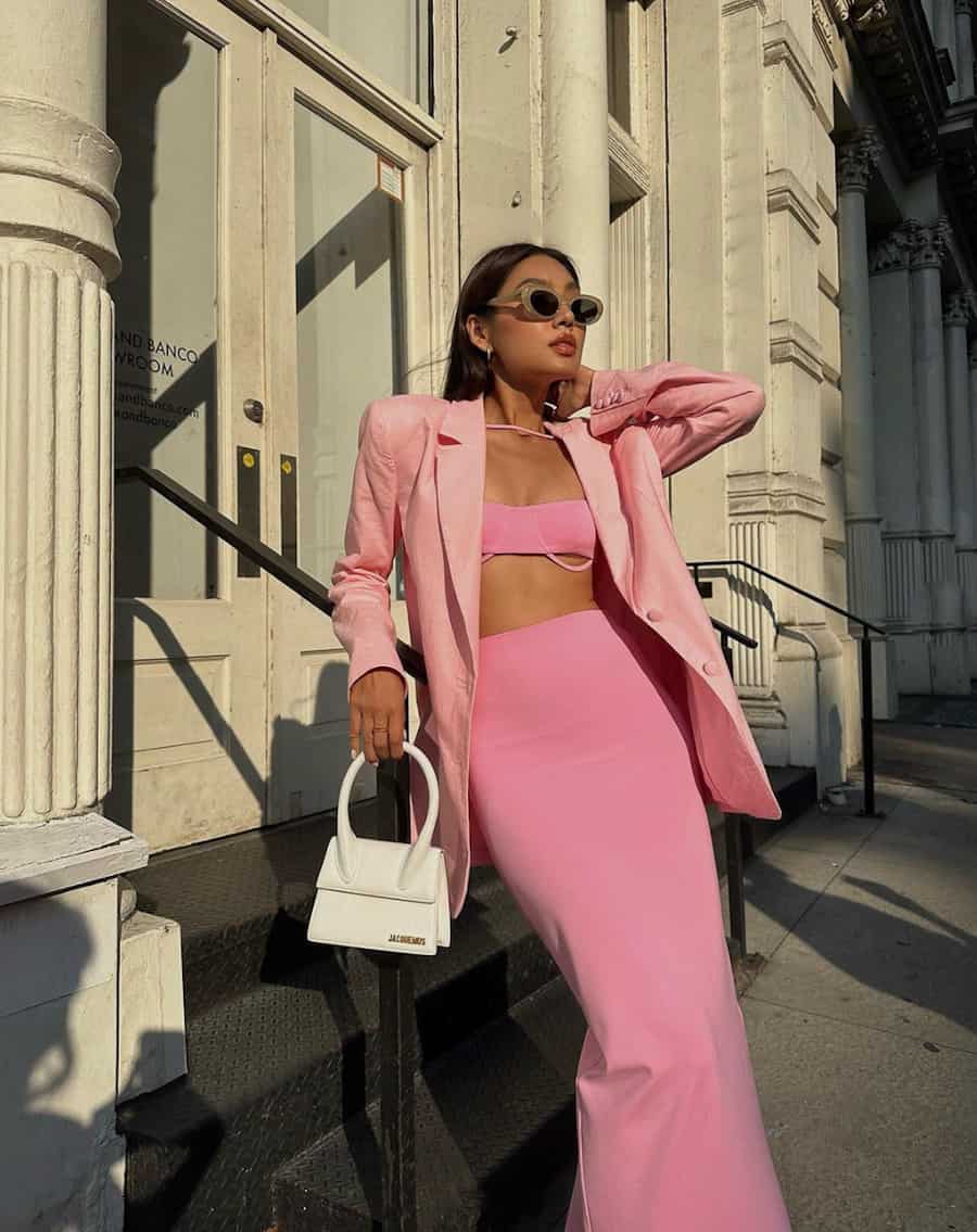 woman wearing a pink crop top, pink skirt, and pink blazer with a small white handbag