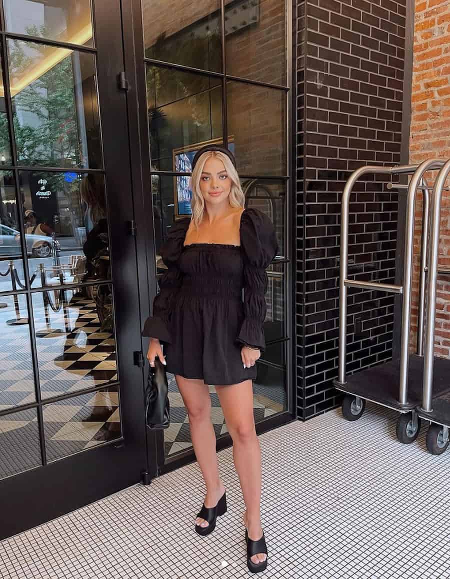 woman wearing a black mini dress with long puff sleeves and black chunky heel sandals