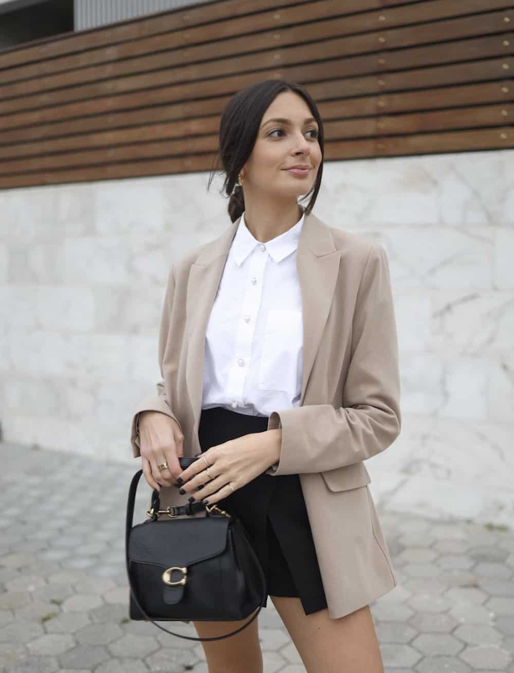 Woman wearing black shorts, a white button down and a tan blazer.