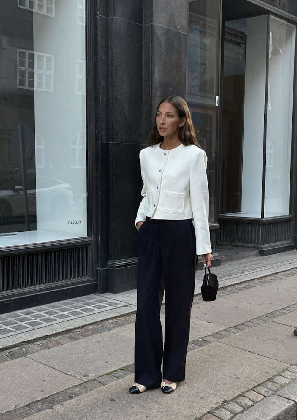 Woman wearing black trousers and a white cropped coat.