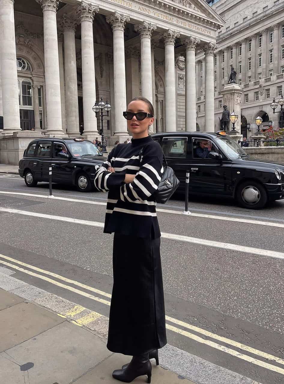 woman in a striped knit sweater, black midi skirt, and ankle boots