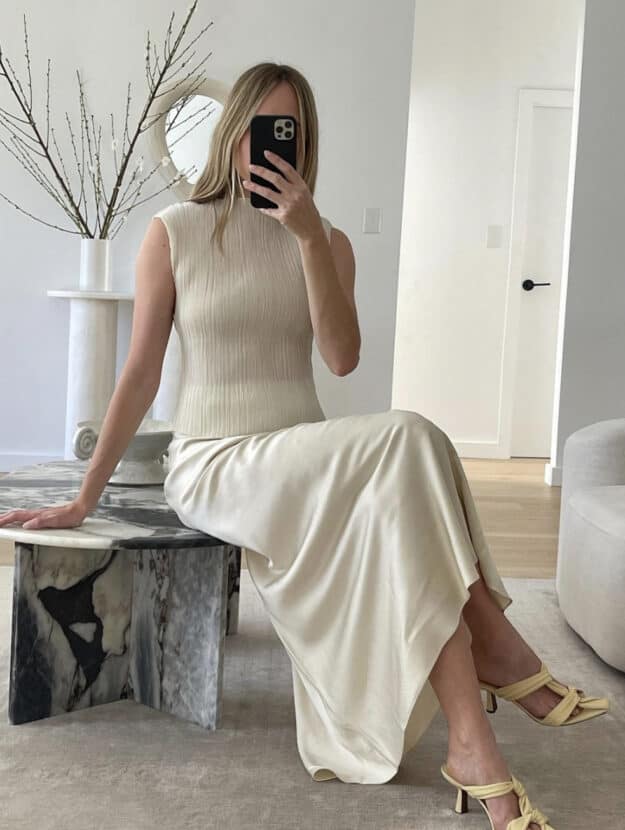 Woman wearing a cream silk midi skirt and a cream tank with heels.