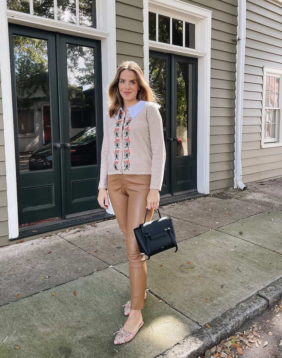 woman in a knit cardigan with floral details and light brown leather pants with flats