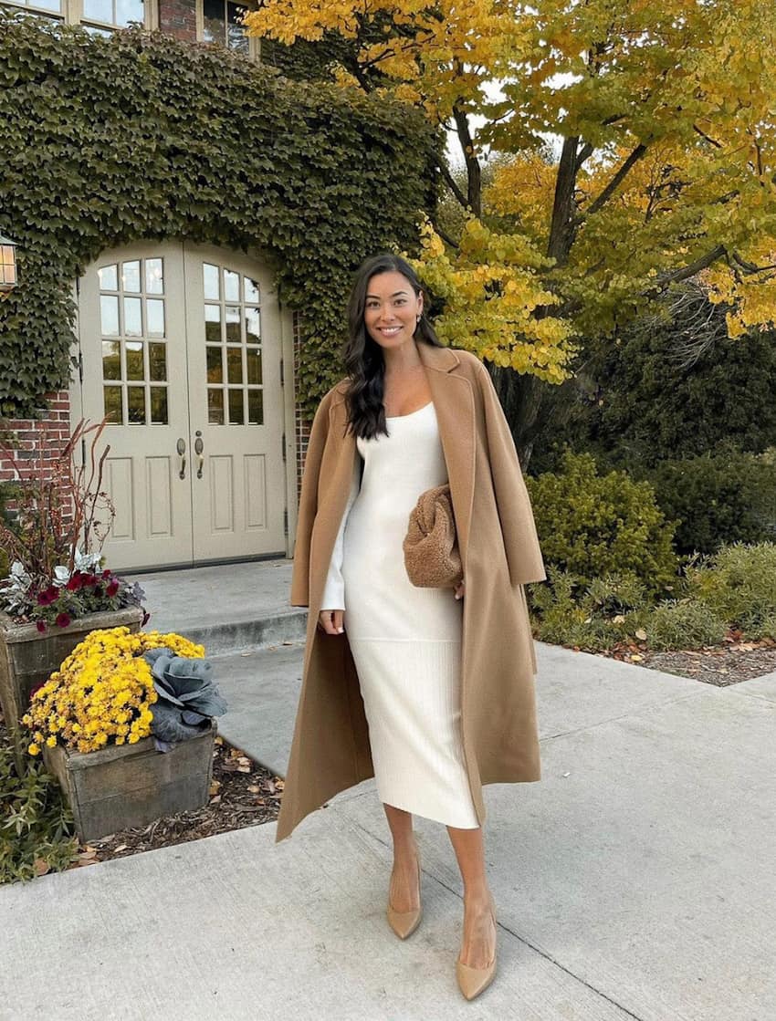 woman in a long ivory sweater dress with a camel coat over her shoulders and heels