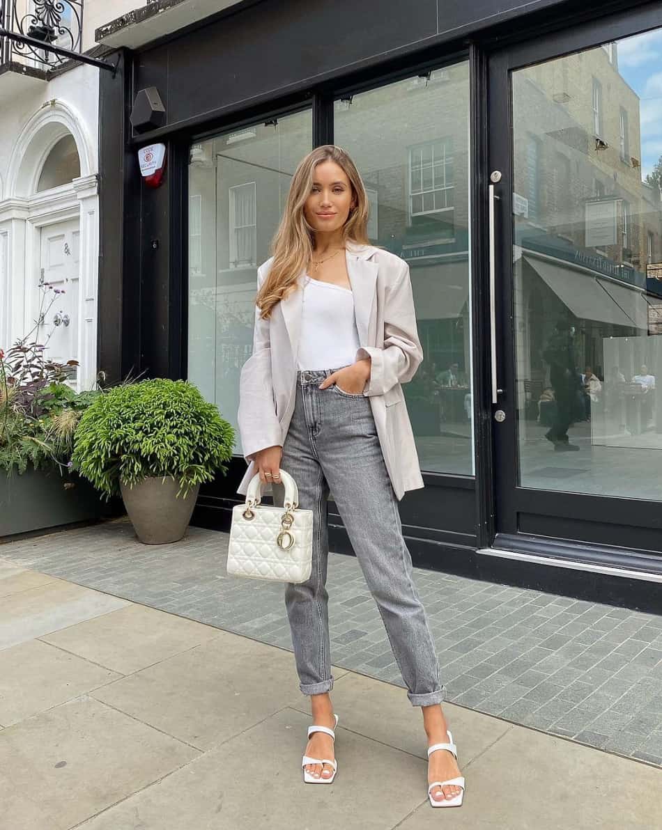 woman wearing a white bodysuit with a blazer, grey jeans, and white heels