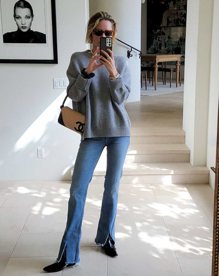 woman wearing a grey sweater with split hem bootcut jeans and black ankle boots