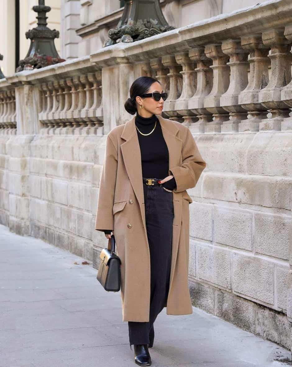 woman wearing a long camel coat over a black sweater and black bootcut jeans with black shoes