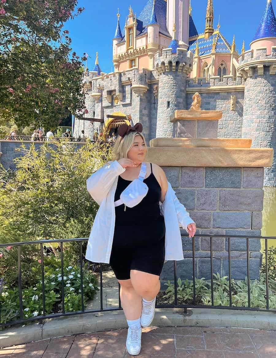 plus-size woman at Disneyland wearing a black spandex romper, sneakers, and a white oversized button up shirt