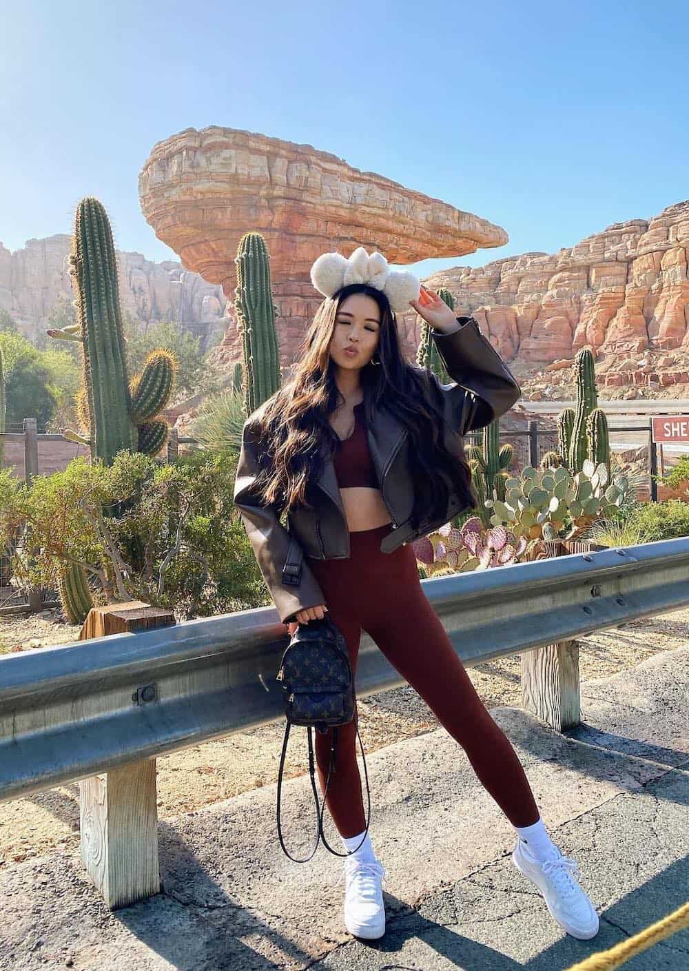 woman at Disneyland wearing a matching leggings and bra set with sneakers and an oversized bomber jacket