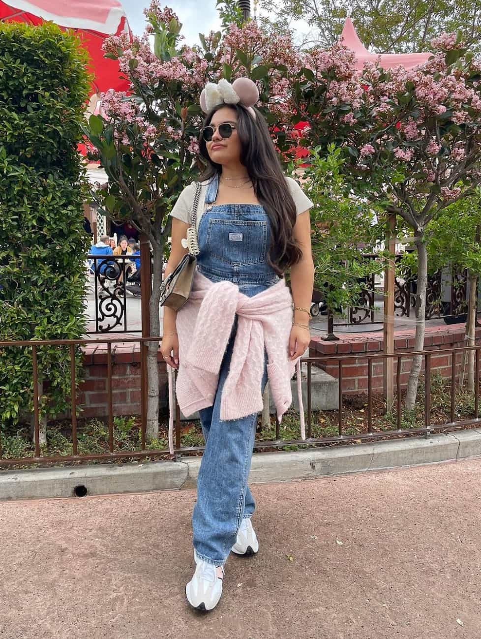 woman wearing a pair of denim overalls with a white t-shirt and sneakers at Disneyland