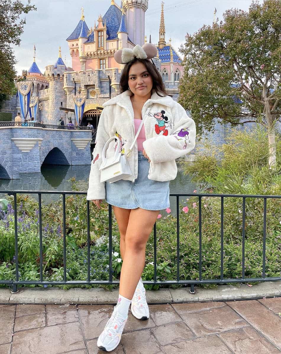 woman at Disneyland wearing a fleece embroidered zip-up jacket, denim skirt, and sneakers