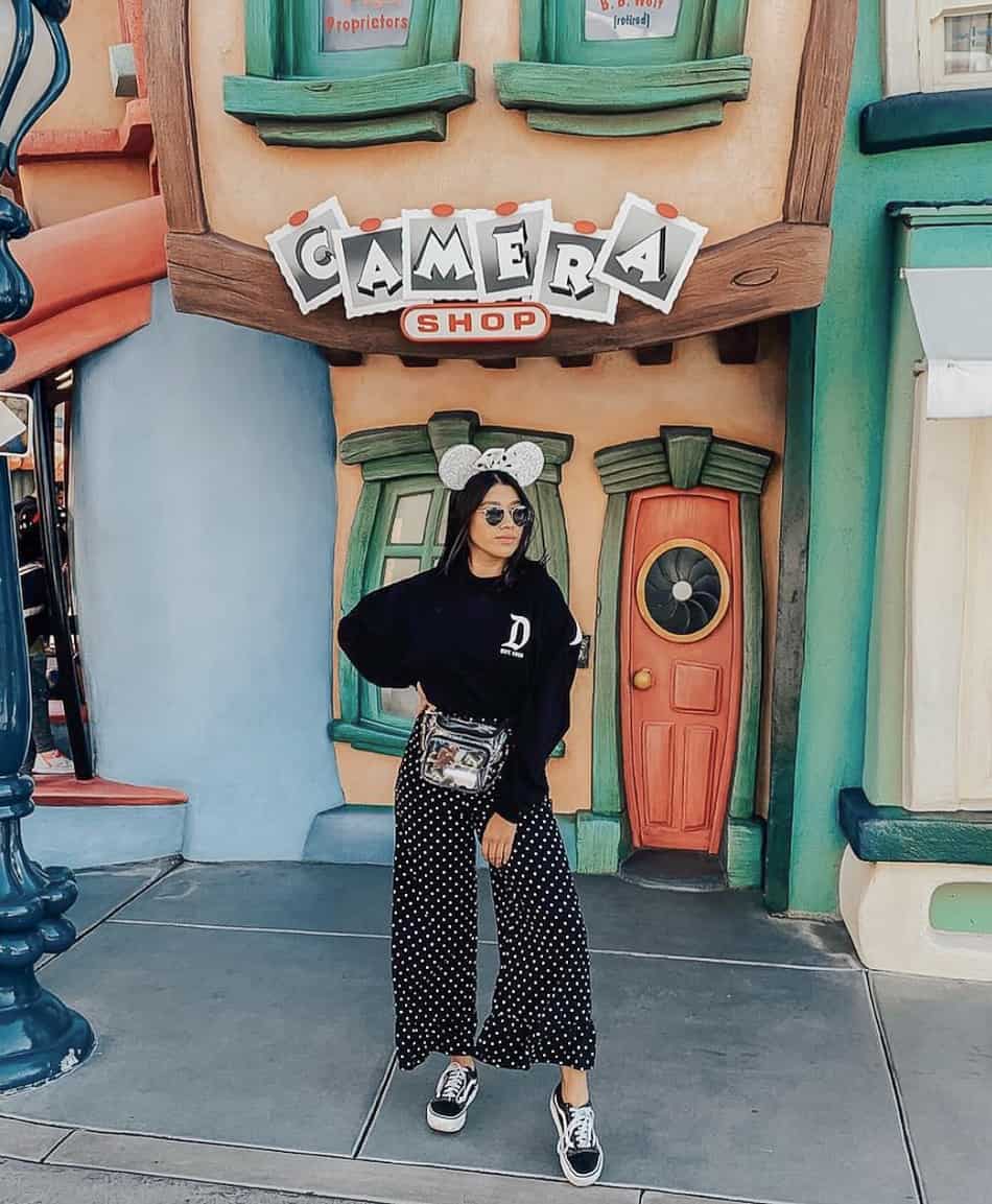 woman at disneyland wearing a black Disney sweater, black polka dot pants, sneakers, and silver glitter Minnie Mouse ears