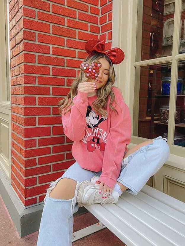 woman at Disneyland wearing Minnie Mouse ears, a pink Minnie sweater and distressed jeans with white sneakers