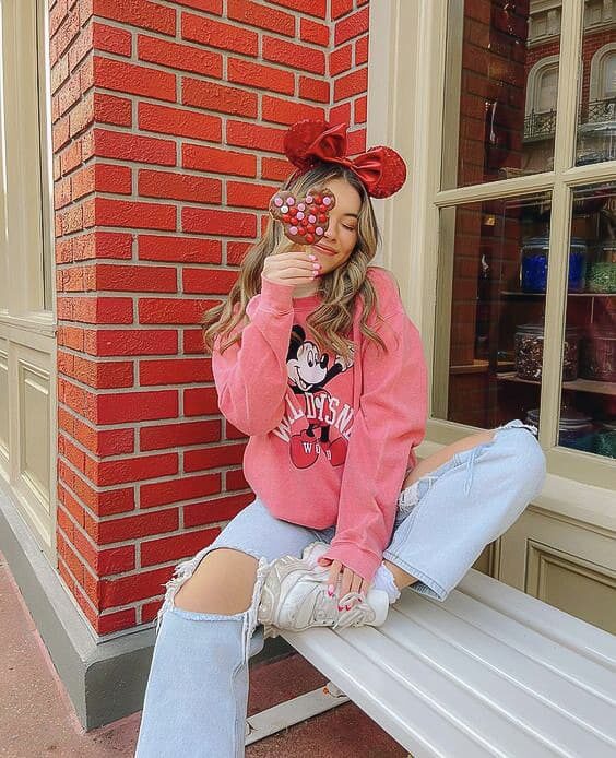 woman at Disneyland wearing Minnie Mouse ears, a pink Minnie sweater and distressed jeans with white sneakers