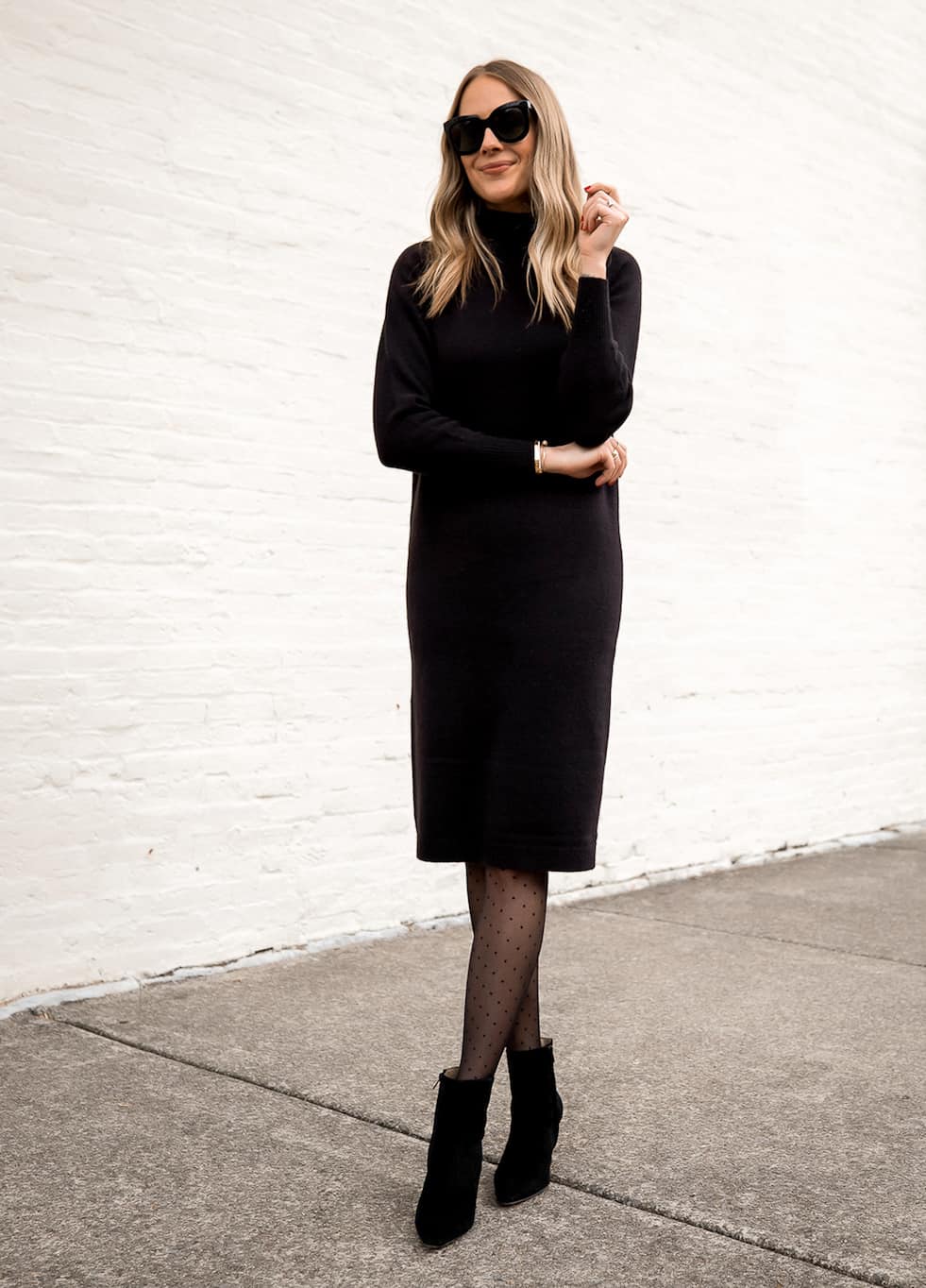 image of a woman wearing a midi length black sweater dress with black sheer polka-dot tights and black ankle boots