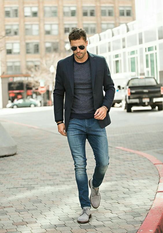 man wearing a navy blazer over a grey shirt with blue jeans and dress shoes