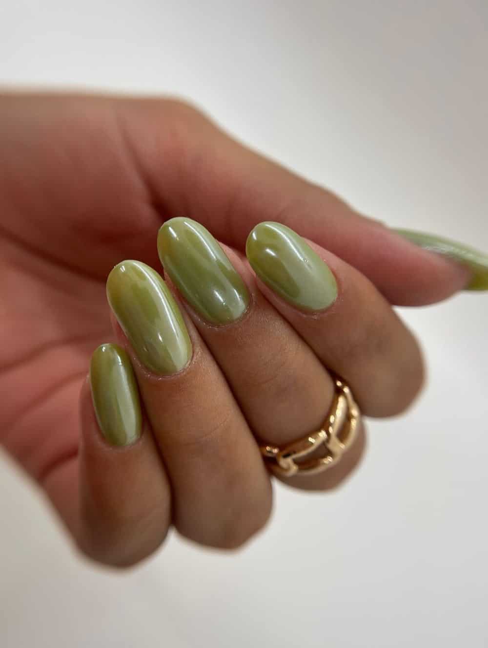 image of a hand with long round nails with light olive green polish and a chrome finish